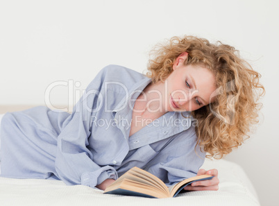 Beautiful blonde woman reading a book while lying on her bed