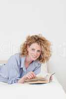 Attractive blonde woman reading a book while lying on her bed