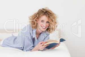 Good looking blonde woman reading a book while lying on her bed