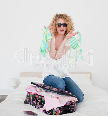Attractive blonde female trying to close her suitcase in her bed