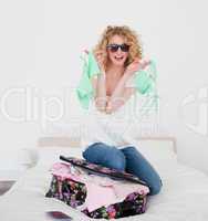 Attractive blonde female trying to close her suitcase in her bed