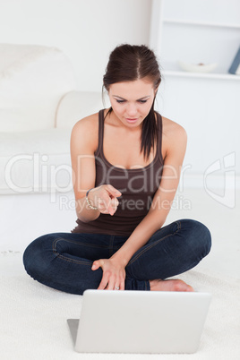 Surprised dark-haired woman pointing at her laptop