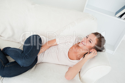 Smiling brunette calling while lying on her sofa Smiling brunette calling while lying on her sofa