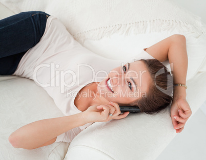 Close up of a smiling brunette calling while lying on her sofa