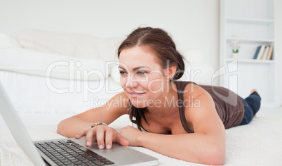 Young woman lying on a carpet with a laptop