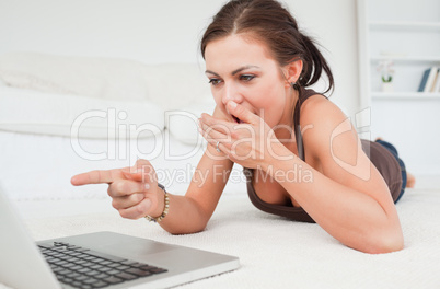 Cute brunette lying on a carpet with a laptop