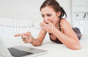 Cute brunette lying on a carpet with a laptop