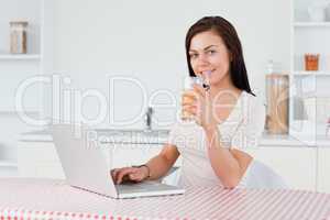 Young woman using her laptop and drinking orange juice