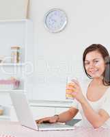 Portrait of a brunette using her laptop and drinking juice