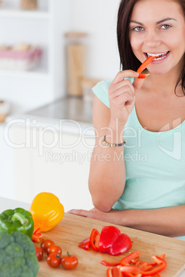 Portrait of a cute brunette eating a slice of pepper