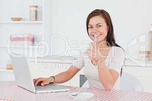 Charming brunette using her laptop and having a tea