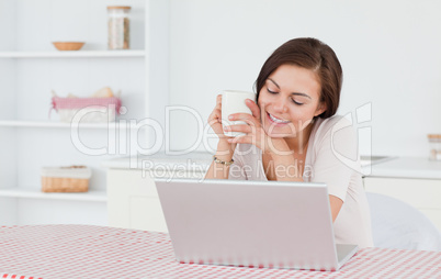 Cute brunette using her laptop and having a tea