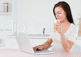 Brunette using her laptop and drinking orange juice