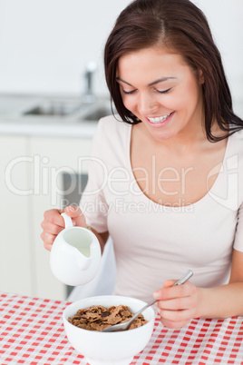 Portrait of a smiling brunette pouring milk in her cereal