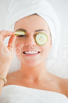 Young woman with a knowing smile with cucumber slices on the fac