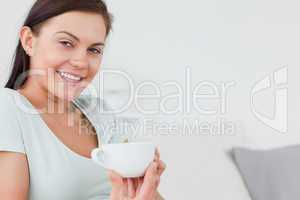 Close up of a brunette sitting on a sofa with a cup of coffee