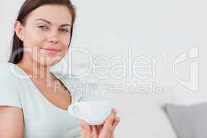 Close up of a charming woman sitting on a sofa with a cup of tea