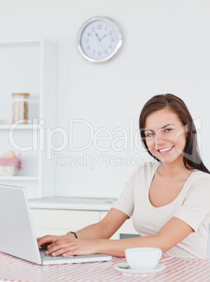 Smiling brunette using her laptop and having a tea