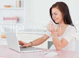 Dark-haired woman using her laptop and having a tea