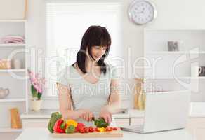 Happy brunette woman cooking while relaxing with her laptop