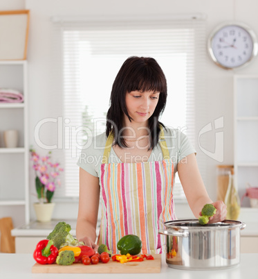 Pretty brunette woman posing while cooking vegetables