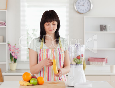 Good looking brunette woman pealing a banana while standing