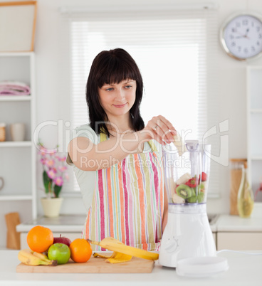 Attractive brunette woman putting vegetables in a mixer while st