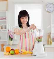 Attractive brunette woman putting vegetables in a mixer while st