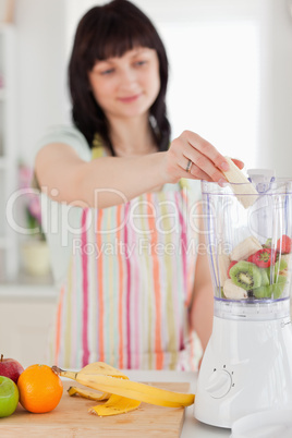 Charming brunette woman putting vegetables in a mixer while stan