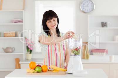 Gorgeous brunette woman putting vegetables in a mixer while stan