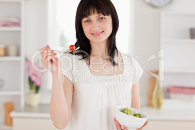 Attractive brunette female eating a cherry tomato while holding