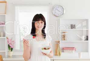 Good looking brunette female eating a cherry tomato while holdin