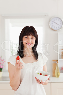 Pretty brunette female eating a cherry tomato while holding a bo