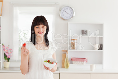Charming brunette female eating a cherry tomato while holding a