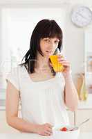 Charming brunette drinking a glass of roange juice while standin