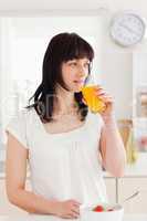Beautiful brunette drinking a glass of orange juice while standi