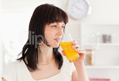 Good looking brunette drinking a glass of orange juice while sta