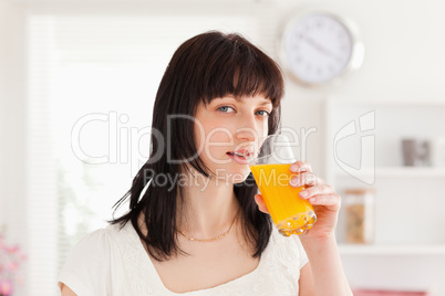 Pretty brunette drinking a glass of orange juice while standing