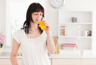 Lovely brunette drinking a glass of orange juice while standing