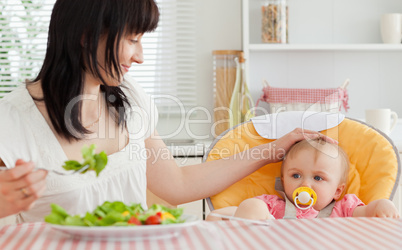 Good looking brunette woman eating a salad next to her baby whil