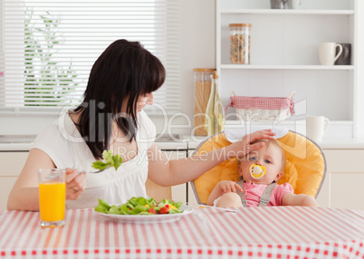 Gorgeous brunette woman eating a salad next to her baby while si
