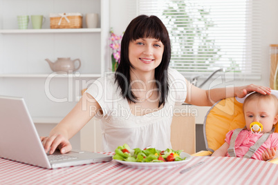 Attractive brunette woman eating a salad next to her baby while