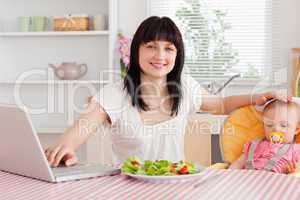 Attractive brunette woman eating a salad next to her baby while