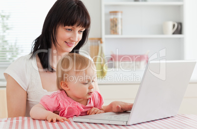 Good looking brunette woman showing her laptop to her baby while