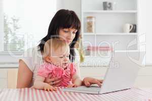 Attractive brunette woman showing her laptop to her baby while s