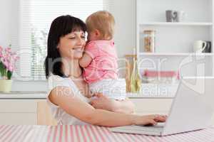 Pretty brunette woman relaxing with her laptop next to her baby