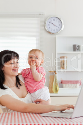 Charming brunette woman relaxing with her laptop next to her bab