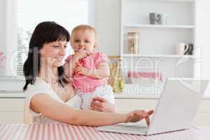 Cute brunette woman relaxing with her laptop next to her baby wh