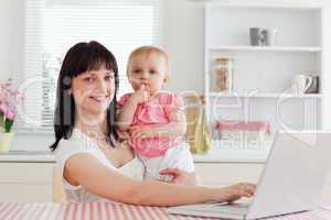 Lovely brunette woman relaxing with her laptop next to her baby
