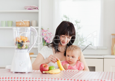 Cute brunette woman showing a banana to her baby while sitting